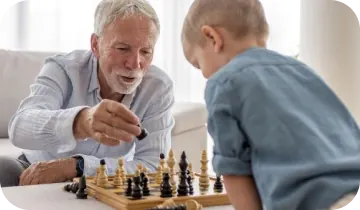 An older man with a white beard playing chess with a young child